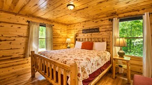 Een slaapkamer in een houten chalet, met een bed, nachtkastjes en een raam met gordijnen.