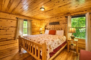 Ein Schlafzimmer einer Holzhütte mit Bett, Nachttischen und einem Fenster mit Vorhängen.
