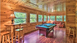 Een houten chaletinterieur met een pooltafel, barstoelen en een bank.