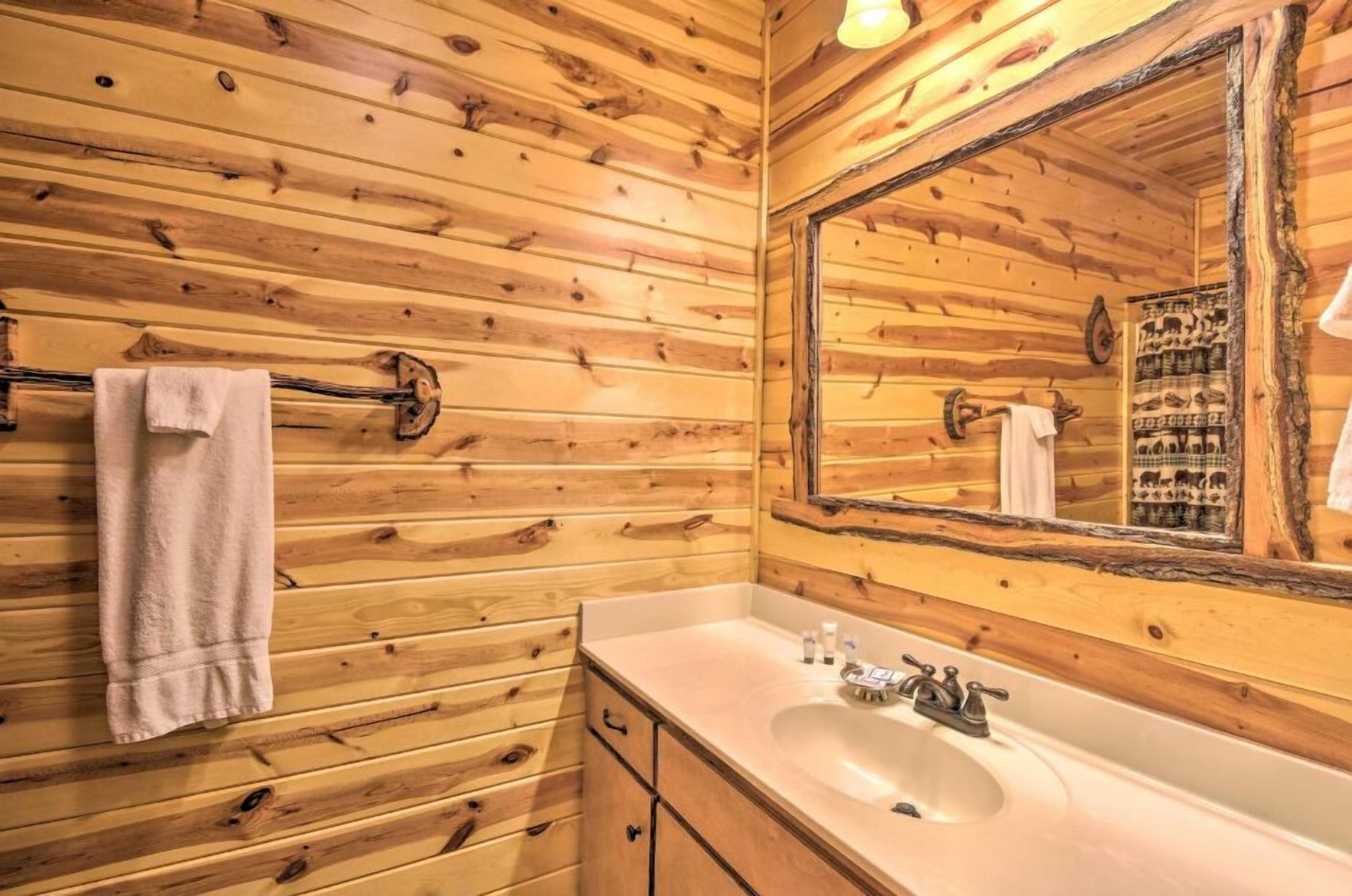 A wooden cabin bathroom with a large mirror, a sink, and a towel hanging on a rack.