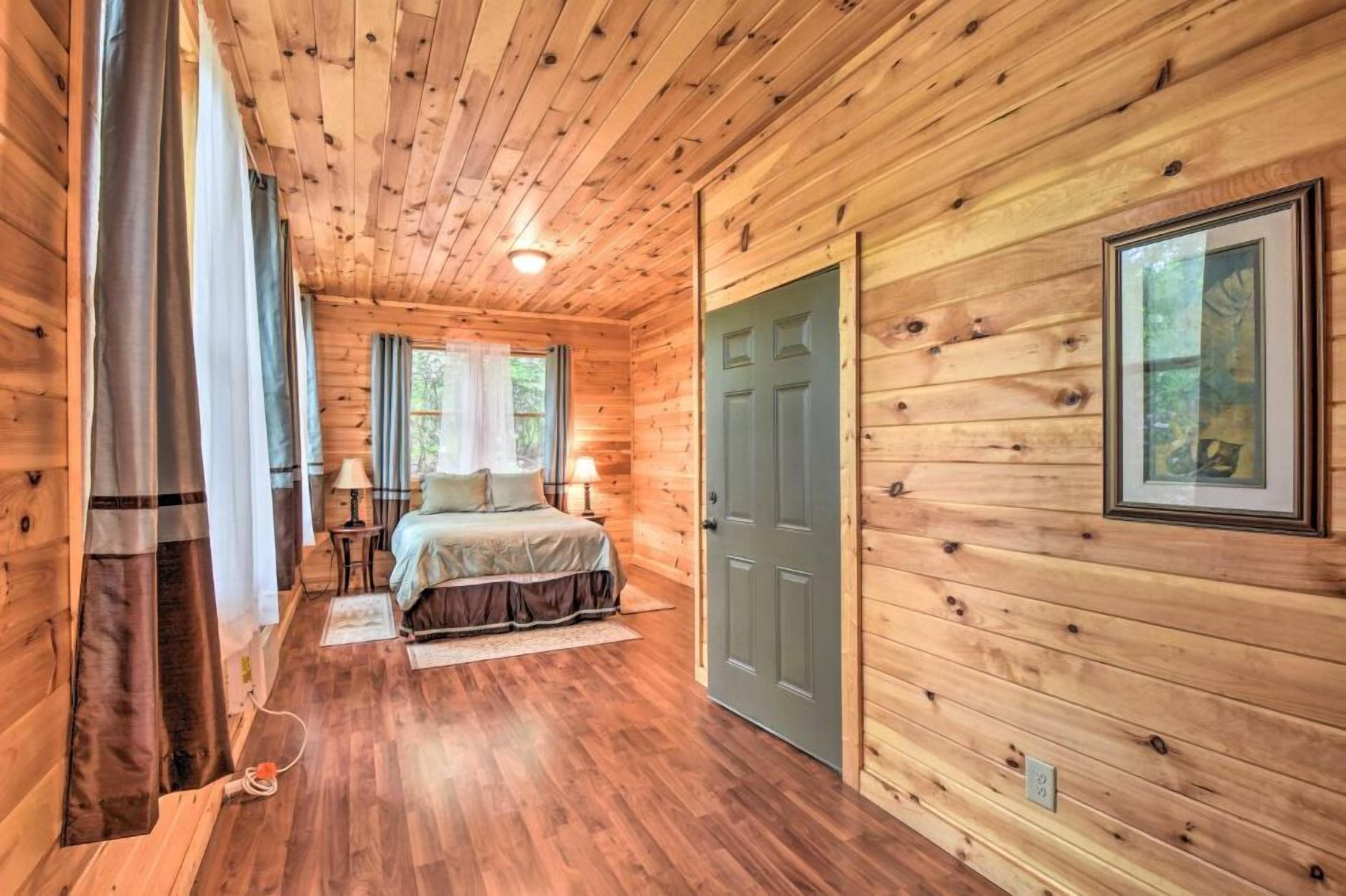 A wooden cabin bedroom with a bed, a nightstand, a lamp, and a door.