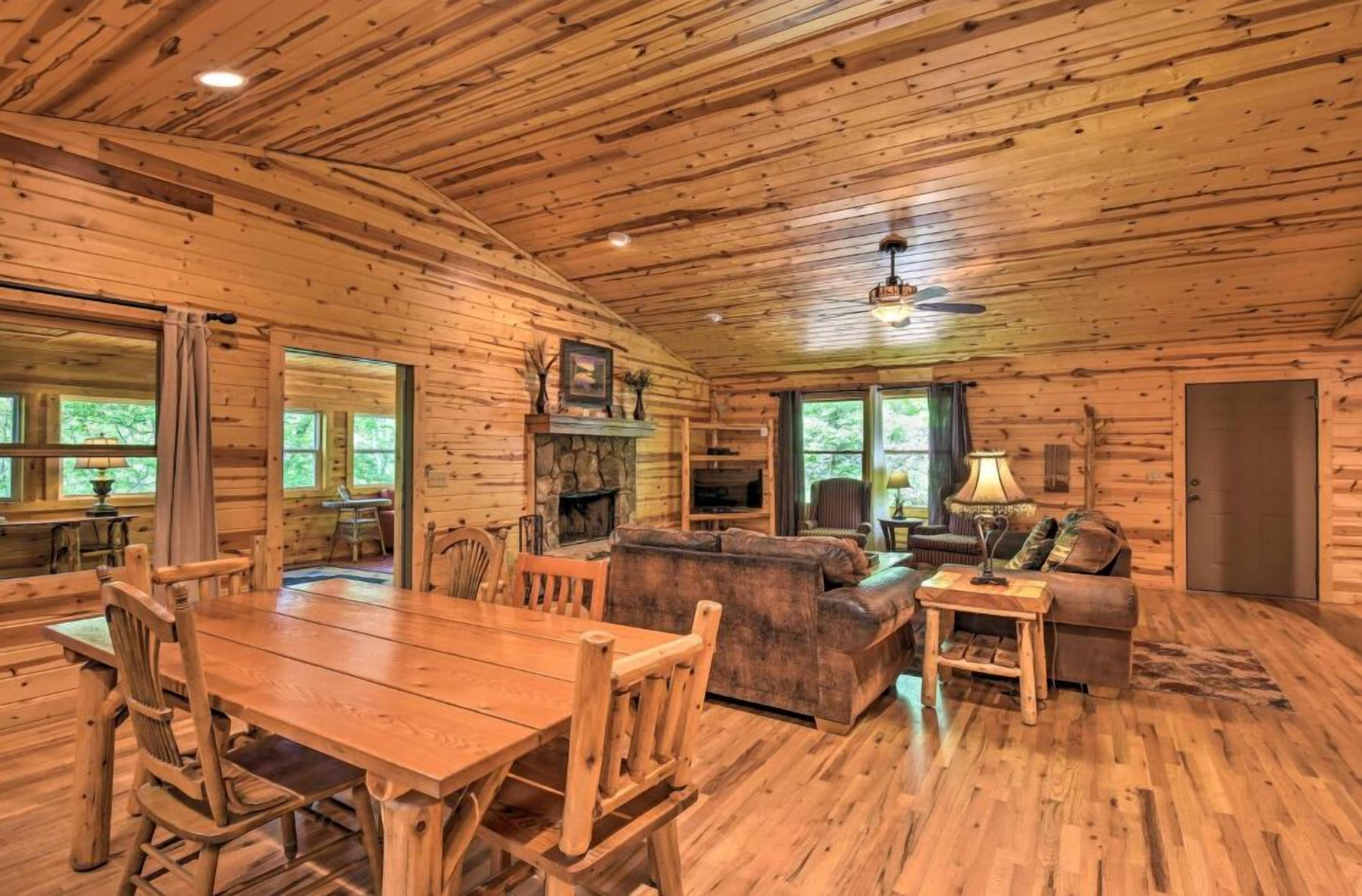 A wooden cabin interior with a dining table, chairs, a sofa, and a fireplace.