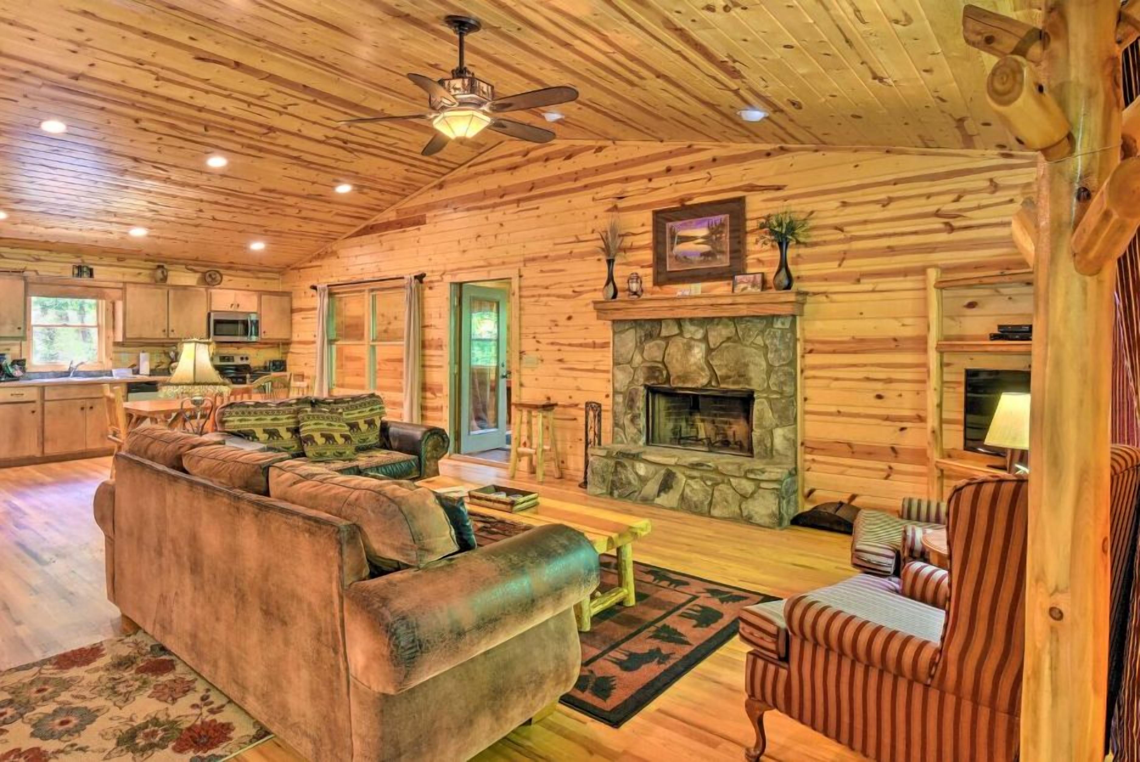 A log cabin interior with a fireplace, a sofa, a striped armchair, and a dining area.