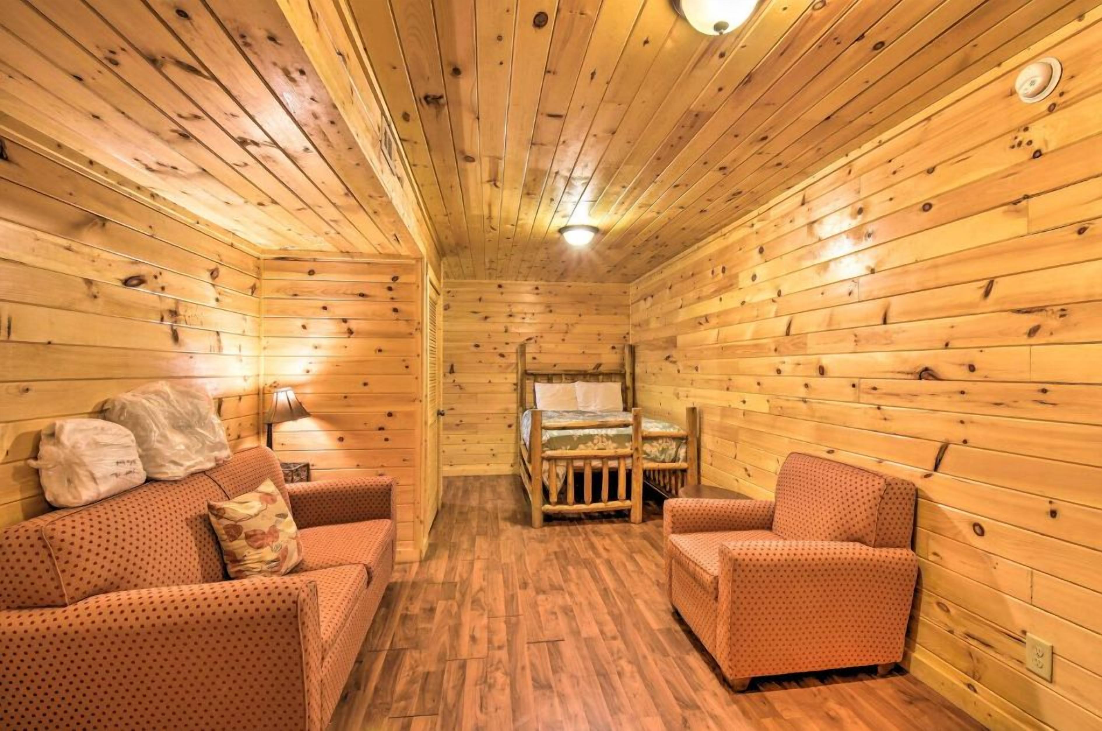 A wooden cabin interior with a sofa, armchairs, a bed, and a lamp.
