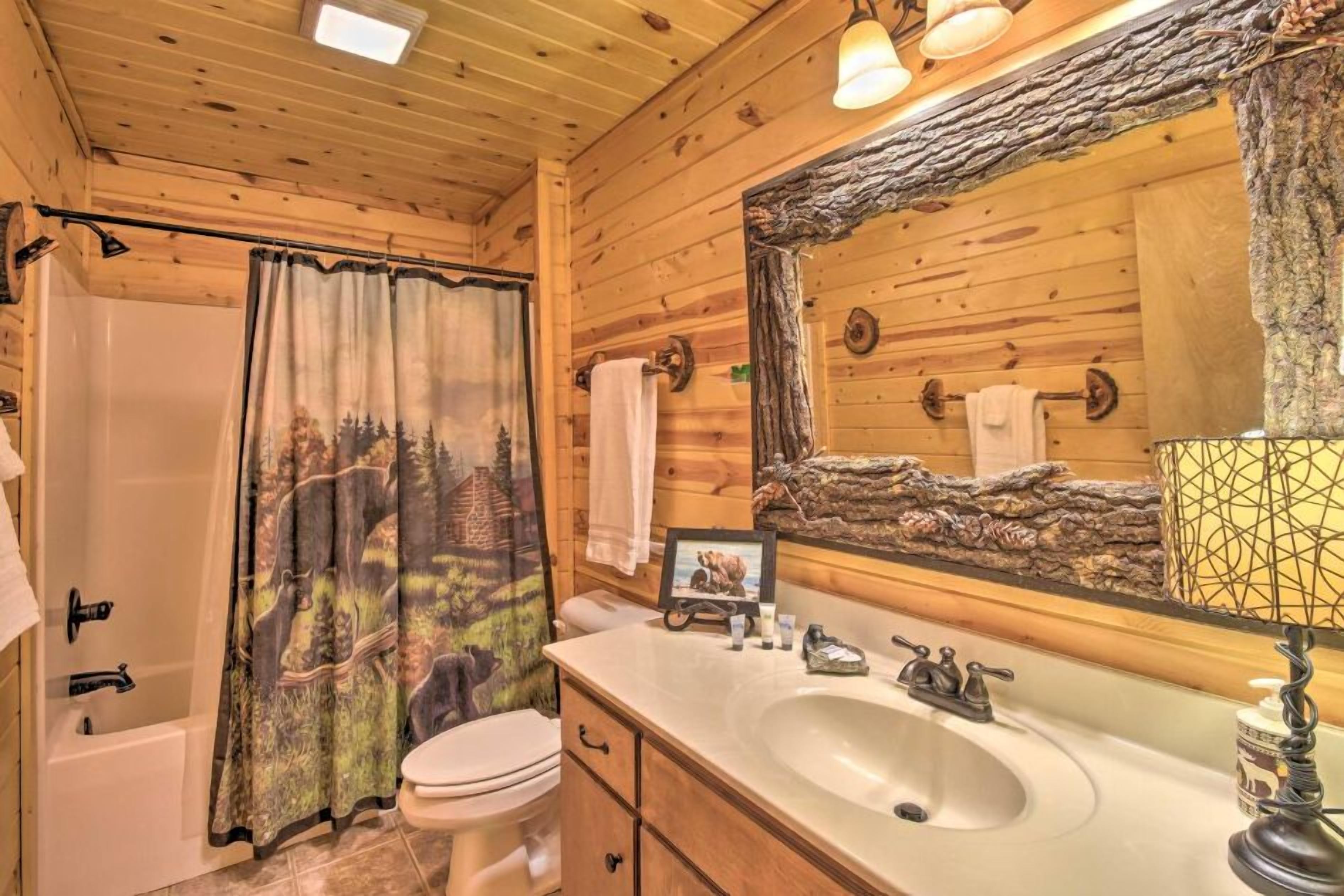 A wooden cabin bathroom with a bathtub, toilet, sink, and a large mirror with a rustic frame.