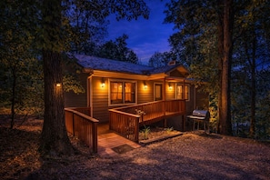 A cabin with a wooden deck, a barbecue grill, and a porch with railings.