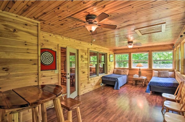 A cabin with wooden walls, a ceiling fan, a bed, a table, and a window.