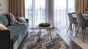 A modern living room with a grey sofa, a round wooden table with a green centerpiece, and a dining area with grey chairs. - PRZY TERMACH - Pokoje Apartamenty Domki (Szaflary)