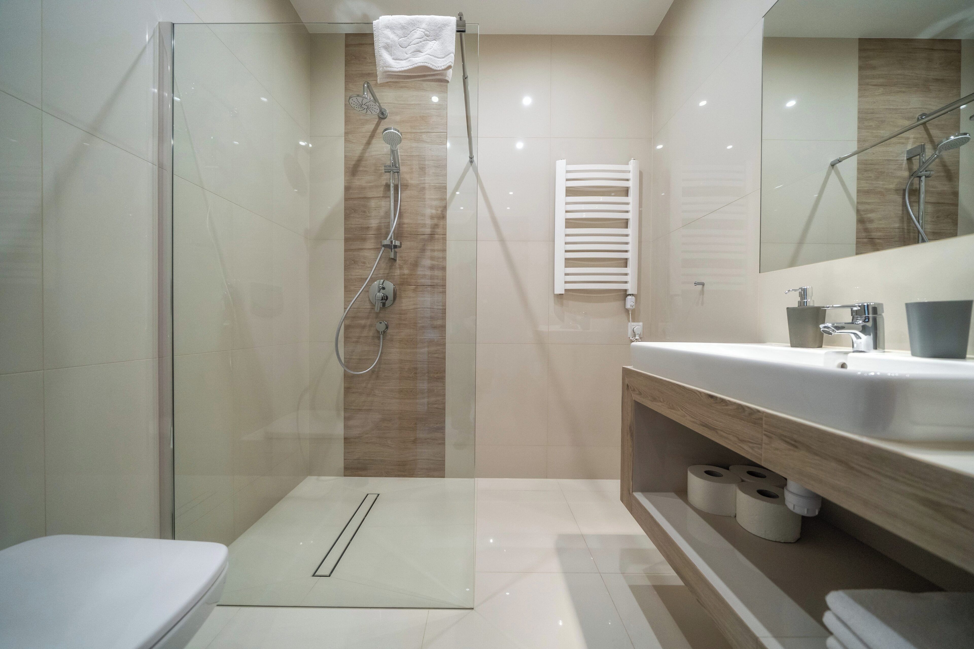A modern bathroom with a glass shower enclosure, a toilet, a sink with a wooden vanity, and a towel rack.