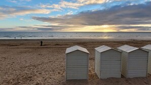 Ein Strand mit drei kleinen, hellen Strandkörben und einer sich entfernten Person.