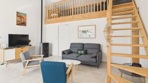 Ein modernes Wohnzimmer mit Schlafkoje, Flachbildfernseher, grauem Sofa und einer Holztreppe.