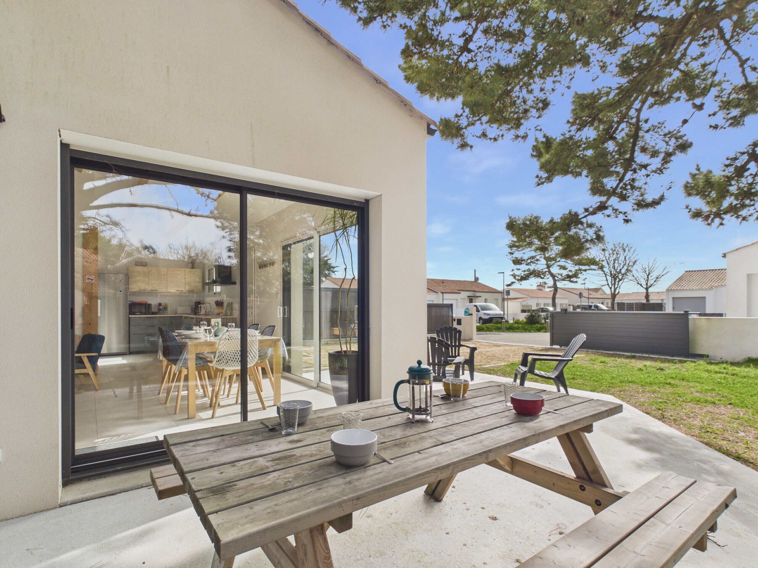 A patio with a wooden table and chairs, a glass door leading to a kitchen, and a view of a residential area.