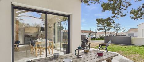 A patio with a wooden table and chairs, a glass door leading to a kitchen, and a view of a residential area.