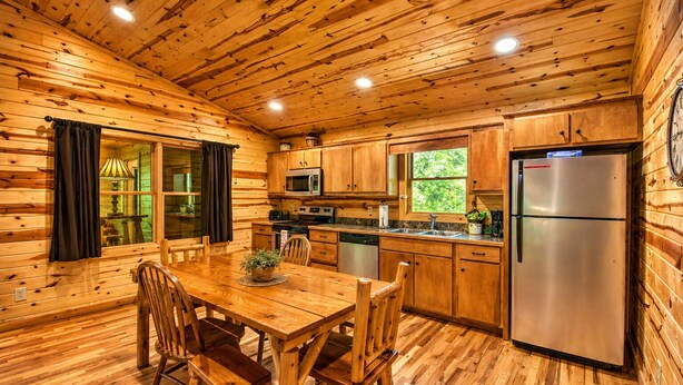 Ein Holzblockhaus-Interieur mit Esstisch, Stühlen, einer Küche inklusive Kühlschrank, Mikrowelle und Spüle.