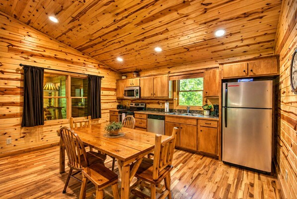A wooden cabin interior with a dining table, chairs, a kitchen with a refrigerator, microwave, and sink. - Roundabout Cabin! Pool Table! Close to Helen! (Clarkesville)