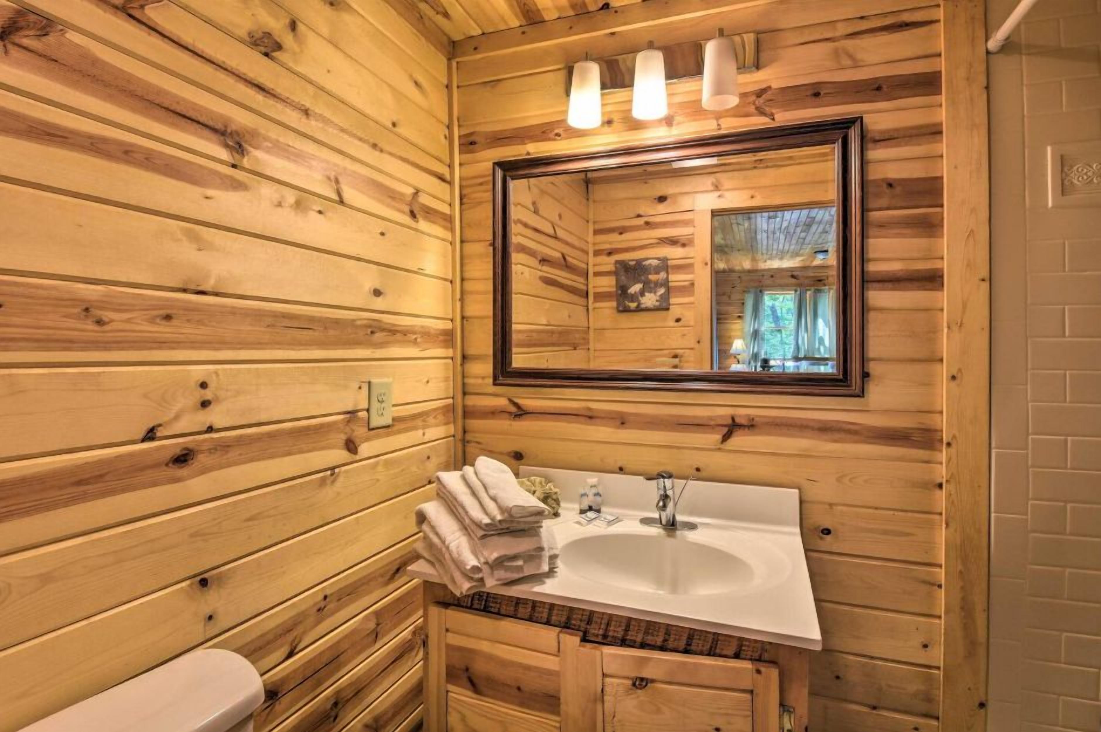A wooden cabin bathroom with a large mirror, a sink, and a toilet.