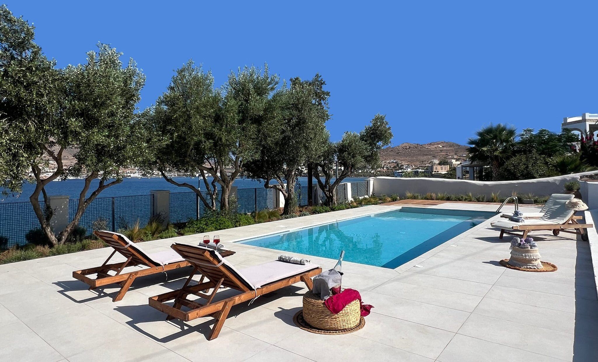A poolside area with lounge chairs, a small pool, and a view of the sea and hills.
