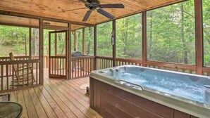 Een houten terras met een jacuzzi, grote ramen en een plafondventilator.