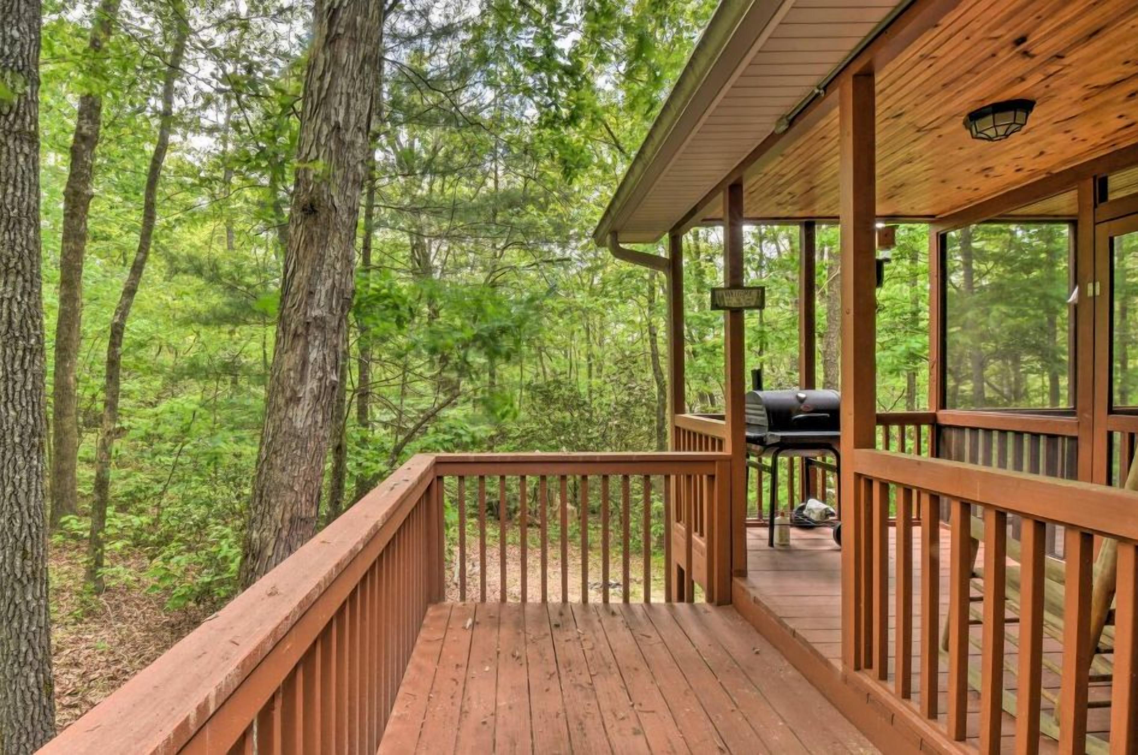 A wooden deck with a grill and a sign, surrounded by dense forest.