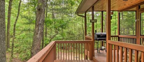 A wooden deck with a grill and a sign, surrounded by dense forest.