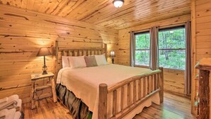 Een slaapkamer in een houten blokhut met een bed, twee bedlampen, een nachtkastje en een raam met gordijnen.