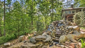 Un pont de pierre rustique, situé dans une zone boisée, avec une cabane en arrière-plan.