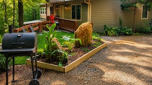 Une maison avec un porche, un barbecue et un jardin agrémenté de plantes et d’un grand rocher.