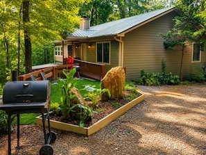 A house with a porch, a barbecue grill, and a garden with plants and a large rock. - Ridgeline Cabin close to Helen, Hiking & Wineries! (Clarkesville)