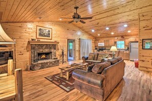 A log cabin interior with a stone fireplace, wooden furniture, and a kitchen area. - Ridgeline Cabin close to Helen, Hiking & Wineries! (Clarkesville)