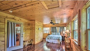 Une chambre dans un chalet en bois, avec un lit, un ventilateur de plafond, une fenêtre et une porte.