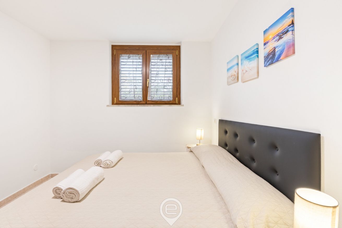 A bedroom with a bed, a window, a nightstand, and wall art.