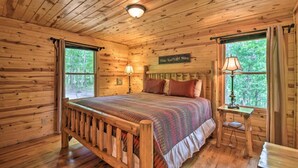A wooden cabin bedroom with a bed, two bedside lamps, a nightstand, and a window with curtains. - 6/5 Valley View! Close to Helen! Near Hiking & Wineries (Clarkesville)
