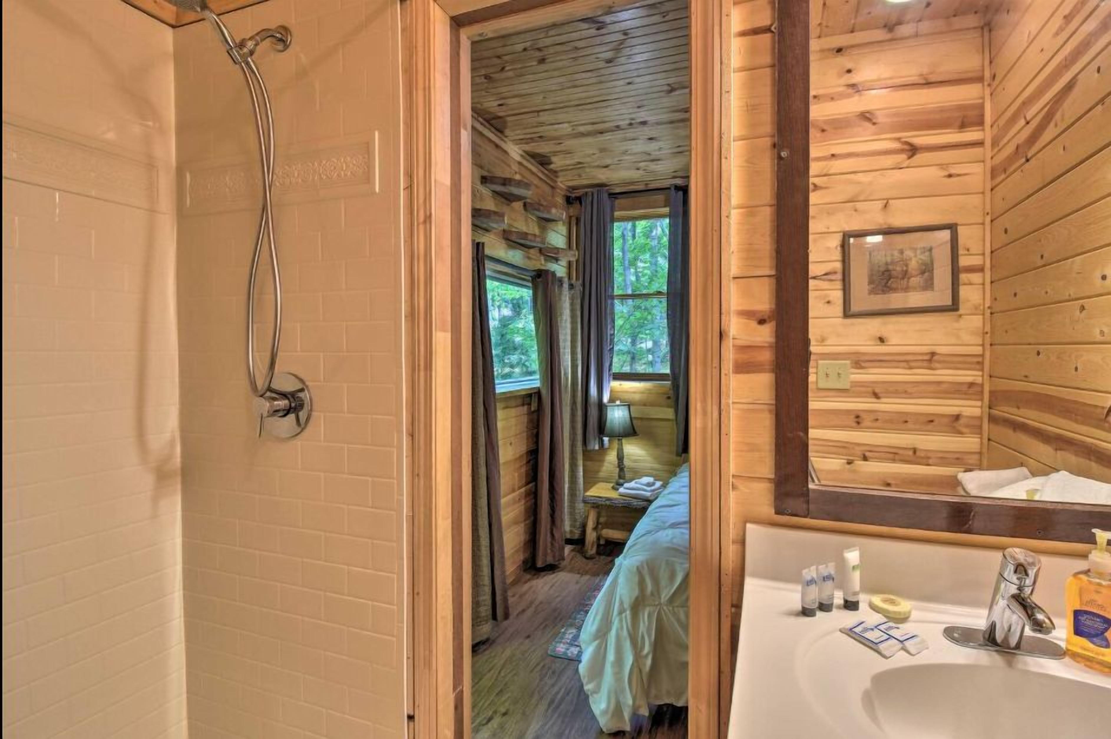A wooden cabin bathroom with a shower, a bed, a sink, and a window.