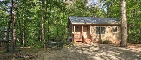A small cabin with a porch, surrounded by trees.