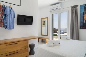 Ein modernes Hotelzimmer mit Bett, Schreibtisch aus Holz, Fernseher und Meerblick.