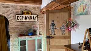 Una habitación rústica con pared de piedra, puerta de madera con decoración de calavera, un mueble pequeño con cajones y una mesa con juegos de mesa.