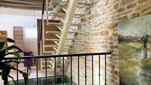 Una escalera con barandillas de cristal, una pared de piedra y un cuadro de paisaje.