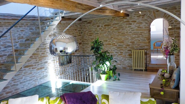 Un interior moderno con una pared de piedra, una escalera de cristal y una zona de estar acogedora con cojines.