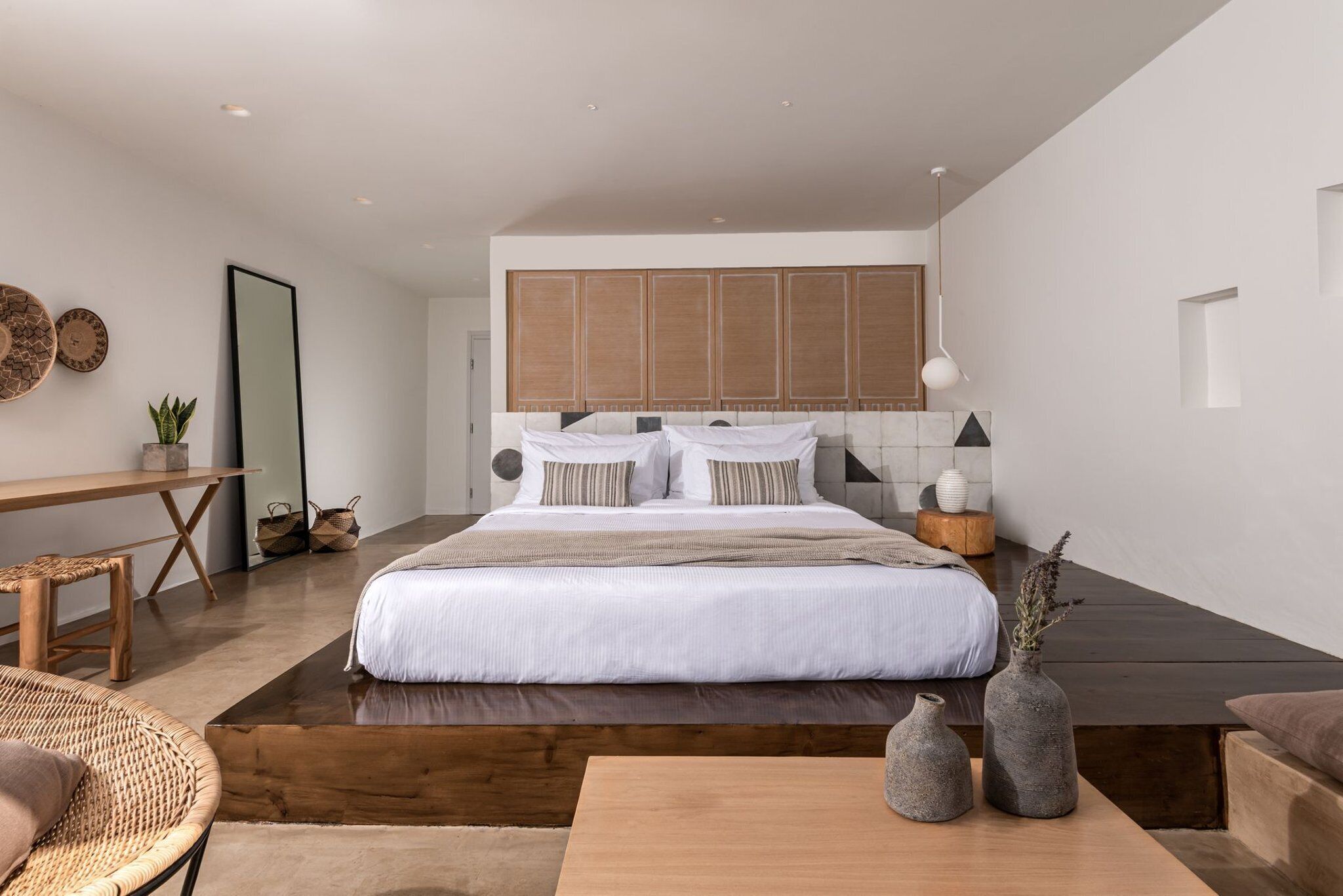 Een moderne slaapkamer met een groot bed, houten nachtkastjes, een bureau en een zithoekje.