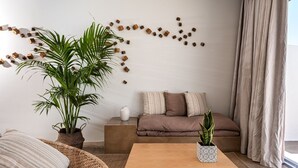 En moderne stue med en sofa, et sofabord, en fletstol og to plantepotteplanter.