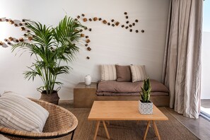 A modern living room with a sofa, a coffee table, a wicker chair, and two potted plants. - Veloria Suite, Divine Sea Views, Infinity Pool, Oia (Santorini)