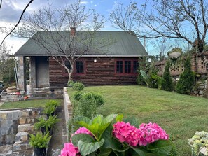 A log cabin with a stone staircase leading to a porch, surrounded by a well-maintained lawn and various plants.