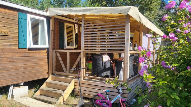 Une cabane en bois avec un porche couvert, des marches menant à une porte et un v élo garé à l’extérieur.