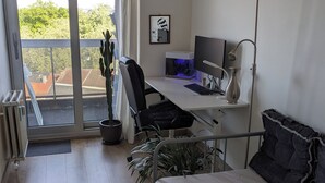 A modern bedroom with a bed, a desk with a computer, a potted plant, and a view of greenery through a sliding door. - Stylish apartment with AC and sweeping views over historic Leuven (Leuven)