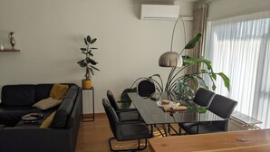 A modern living room with a black sofa, a wooden dining table, and black chairs. There is a potted plant on a small table, and a large window with curtains. - Stylish apartment with AC and sweeping views over historic Leuven (Leuven)