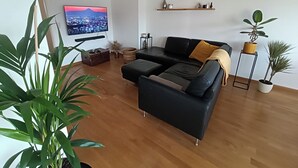A modern living room with a black sofa, wooden floor, a flat-screen TV, and various plants. - Stylish apartment with AC and sweeping views over historic Leuven (Leuven)