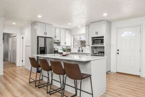 A modern kitchen with white cabinetry, a central island with bar stools, a refrigerator, a microwave, and a sink.