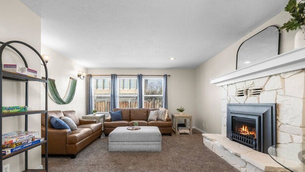 A living room with a stone fireplace, a leather sofa, a coffee table, and a bookshelf. - Cozy Orem House | Playground | Game Rm | Bunk Rm (Orem)