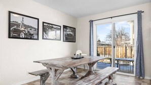 A dining area with a rustic wooden table and benches, a window with a view of a backyard, and three black-and-white photographs on the wall. - Cozy Orem House | Playground | Game Rm | Bunk Rm (Orem)