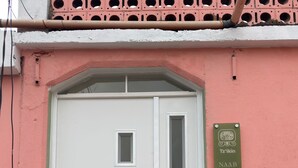 A white door with a glass panel and a metal handle, set in a pink building with a metal railing in front. - Naab Apart Complex (Panajachel)
